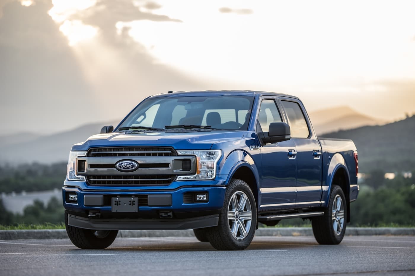 Blue Ford F-150 pickup parked on a road with hills behind