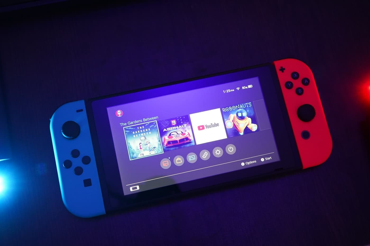 Nintendo Switch in handheld mode with red and blue Joy-Cons, home screen on